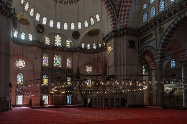 Istanbul, Turkey - 1 March 2021. Rich interior of the Suleymaniye mosque in Istanbul. Bright luminous windows with mosaics and a lot of glass candles lanterns hang on huge chandeliers. 