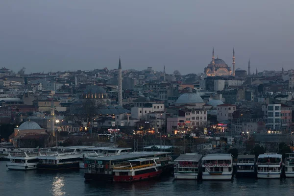 Dark evening urban landscape of the Istanbul embankment of Eminonu district in the Golden Horn Bay. Sea transport is moored at the pier. Many mosques and its high minarets are visible in the dusk.