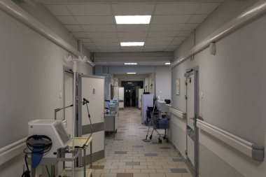 The hospital corridor of a Russian hospital. The doors to the wards are open, with a nurse's station between them. Medical equipment along the grey walls