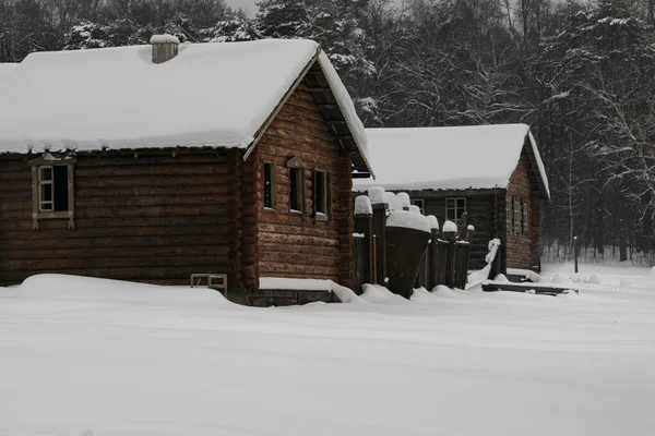 森と雪のドリフトの真ん中に素朴なログハウスのカップルが立っています 家の屋根の上に雪の厚い層があります 雪や雪に覆われた木々がたくさんあります — ストック写真