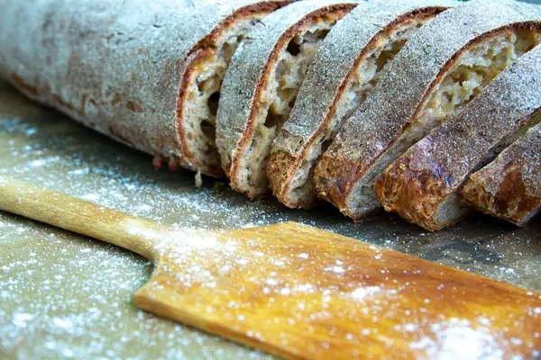 Fresh whole grain sliced bread sprinkled with flour lies on the table — Stock Fotó