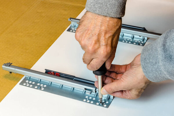Работник прикрепляет современные держатели ящиков к перегородке мебели