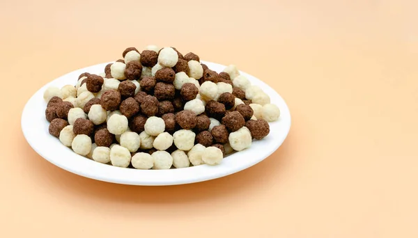 Various chocolate and vanilla flavored cornflakes balls on a white plate on a soft pink background