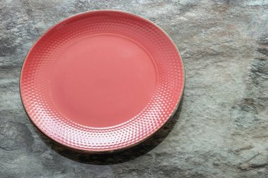 Donuk mermer bir arka planda içi boş, porselen bir kırmızı tabak.