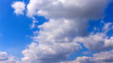 Güneşli bir günde mavi gökyüzünde rüzgarda esen büyük beyaz balon bulutları hızla şekil değiştiriyor.