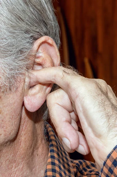 an old man with gray hair in the room puts his finger in his ear