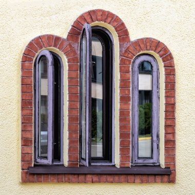 antique wooden window with three arches in yellow wall close up