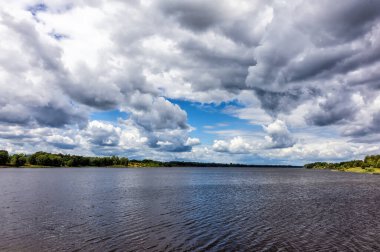 pond landscape surrounded by trees and bushes and cloudy blue sky. Kupiskis. Lithuania. 03. 08. 2022.