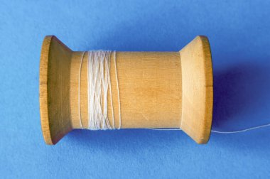 Old almost empty wooden spool of white thread on blue background, top view