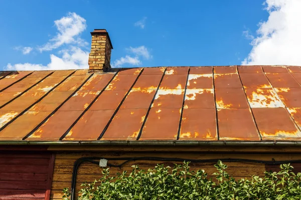Old dilapidated house with rusty tin roof and chimney on sunny day with sky background