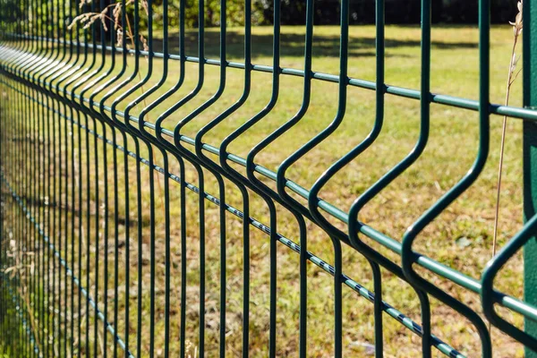 Green segmented welded wire fence outdoors with blurred focus in the distance