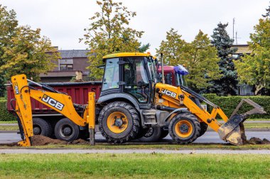 Bir JCB traktör kazıcısı sokağın yakınındaki bir şehir bölgesinde çukur kazıyor ve toprağı bir kamyona boşaltıyor. Panevezy 'ler. Litvanya. - 14. 09 numara. 2022.
