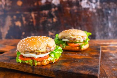 Ahşap bir tahta üzerinde marul, peynir, soğan ve domatesli nefis ev yapımı hamburgerin yakın çekimi.