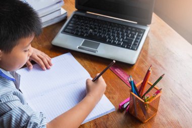 Evdeki tahta masada ödev yapan bir çocuk.