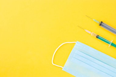 Sarı arkaplanda mavi cerrahi maskeli şırınga.