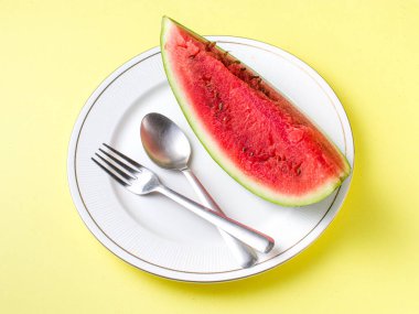 Beyaz tabakta dilimlenmiş karpuz kaşık ve çatal desenli beyaz arka planlı fotoğraf..