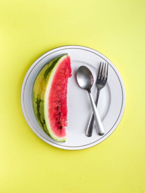 Beyaz tabakta dilimlenmiş karpuz kaşık ve çatal desenli beyaz arka planlı fotoğraf..