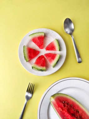 Beyaz tabakta dilimlenmiş karpuz kaşık ve çatal desenli beyaz arka planlı fotoğraf..