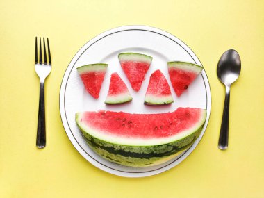 Beyaz tabakta dilimlenmiş karpuz kaşık ve çatal desenli beyaz arka planlı fotoğraf..