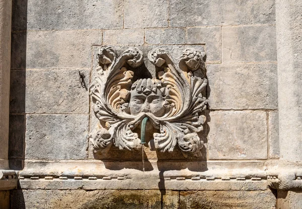 A single mask surronds one of the spigots of Large Onofrio's Fountain in Old Town Dubrovnik