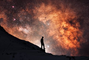 Yıldızlı gece gökyüzünde, tepede bir yürüyüşçünün silueti. Arkasındaki parlak yakın çekim Samanyolu Galaksisi. Derin boşluk.