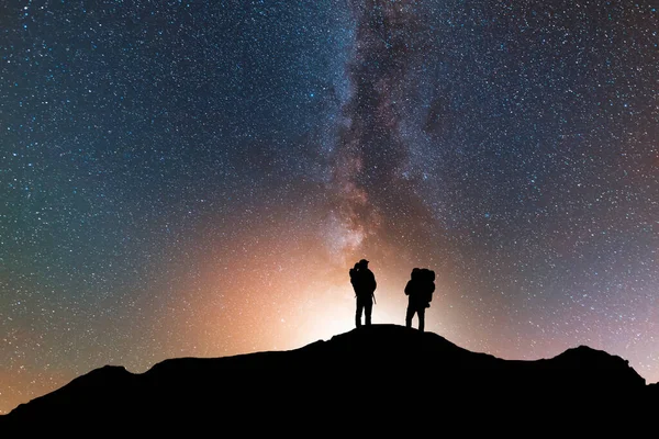 星空の丘の上に2人の旅行者のシルエット 彼の後ろの明るい天の川銀河 ロイヤリティフリーのストック写真