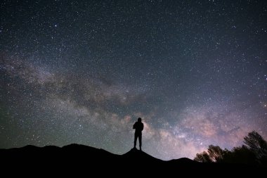 Yıldızlı gece gökyüzünde tepede siluet gezgini. Arkasındaki parlak Samanyolu Galaksisi.
