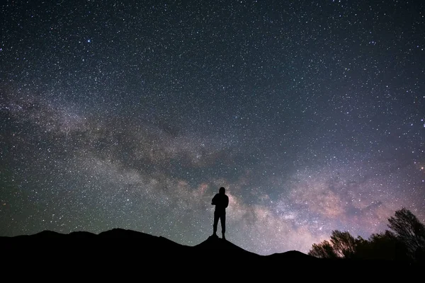 星空の丘の上のシルエットの旅行者 彼の後ろの明るい天の川銀河 ロイヤリティフリーのストック画像