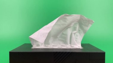 a person's hand pull out a piece of tissue from tissue paper box isolated on green background.
