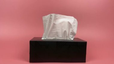 Slow motion, a person's hand pull out a piece of tissue from tissue paper box isolated on pink background.