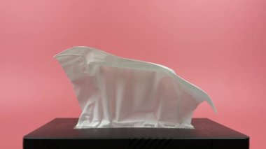 Slow motion, a person's hand pull out a piece of tissue from tissue paper box isolated on pink background.