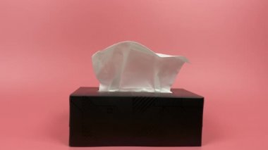 Slow motion, a person's hand pull out a piece of tissue from tissue paper box isolated on pink background.