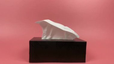 Slow motion, a person's hand pull out a piece of tissue from tissue paper box isolated on pink background.