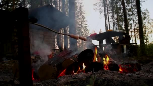Man in the forest fries sausages over the fire — Vídeo de Stock