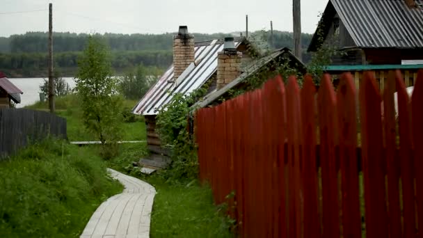 Een houten hek en een dorpshuisje op de achtergrond van de rivier, screensaver — Stockvideo