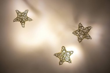 Aydınlatılmış arka planda altın telden örülmüş üç yıldız.