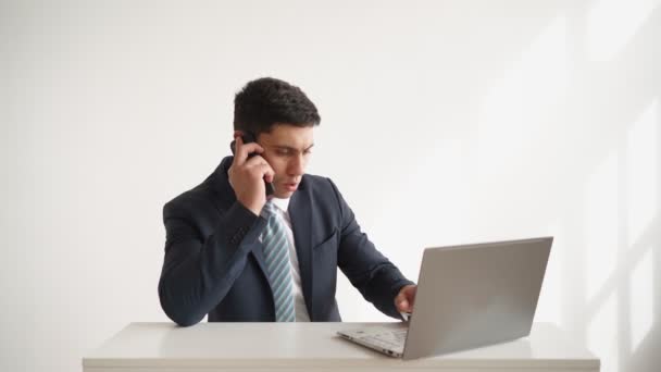 Homem de negócios em desgaste formal trabalha mesa de estar com laptop e falando por telefone — Vídeo de Stock