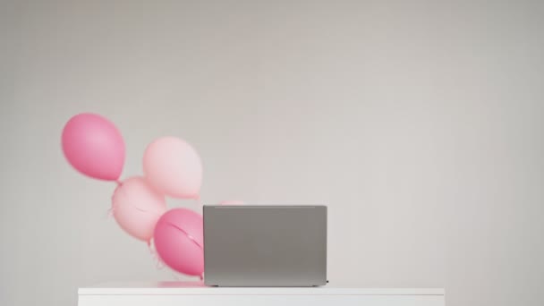 Bureaublad met laptop waarachter feestelijke ballen verschijnen op witte achtergrond — Stockvideo
