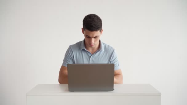 Красивый мужчина в голубой рубашке для поло работает на ноутбуке в офисе на белом фоне — стоковое видео