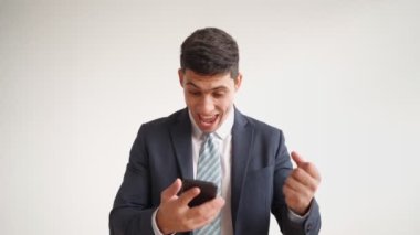 Resmi giysiler içindeki mutlu erkek ofis çalışanı cep telefonuyla zaferi kutluyor.