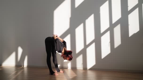 Atletisk kvinde gør yoga og strækker sig på hvid baggrund i lyst sollys – Stock-video
