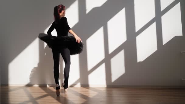 Балерина в черной туту изящно танцует против белой стены в ярком солнечном свете — стоковое видео