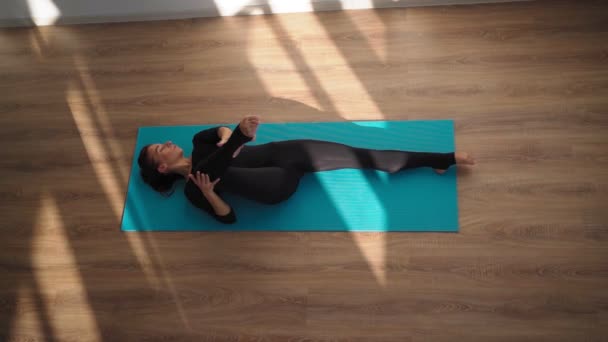 Mujer haciendo yoga y estirándose mientras está acostada en una colchoneta de fitness en casa. Vista superior — Vídeos de Stock