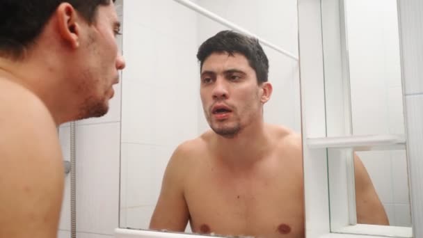 Unavený muž s strništěm na obličeji se umývá v koupelně a dívá se do zrcadla — Stock video