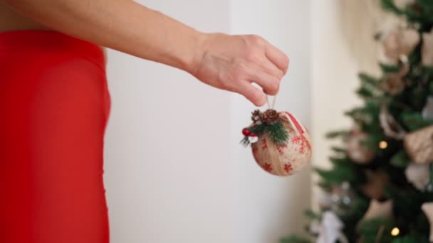 Vrouw versiert kerstboom met feestelijke ballen. Warme lichtjes slingers flikkeren — Stockvideo