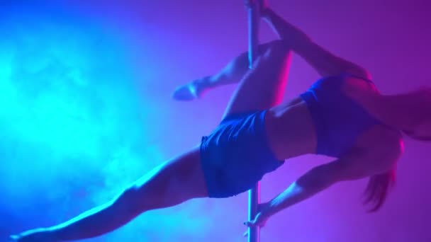 Kvinde pole danser udfører et stunt nummer på pol i et røgfyldt rum i neonlys. – Stock-video