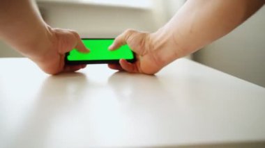 Yakın plan, bir adam masada dururken yeşil ekranlı akıllı telefon kullanır.