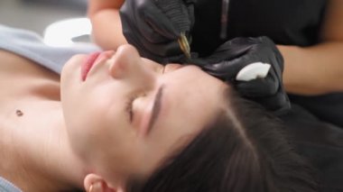 Usta güzellik salonundaki kadına kalıcı kaş makyajı yapıyor..