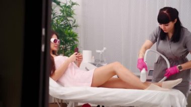 Çekici bir güzellik uzmanı güzel genç bir bayanın bacaklarında lazer tüyü çıkarıyor.