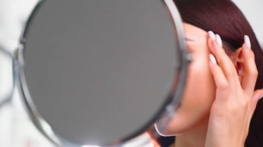 Mükemmel cilt yüzlü güzel bir kadın güzellik salonundaki aynada kendine bakıyor.